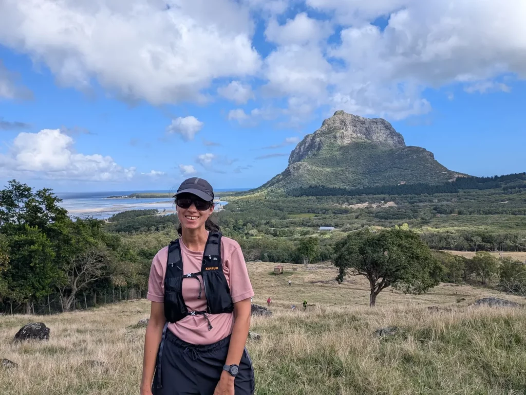 Portrait de Célia Duwicquet en tenue de trail running devant un paysage de savane et de lagon avec en arrière plan la montagne du Morne Brabant à l’Île Maurice, lors du trail de la liberté 2025